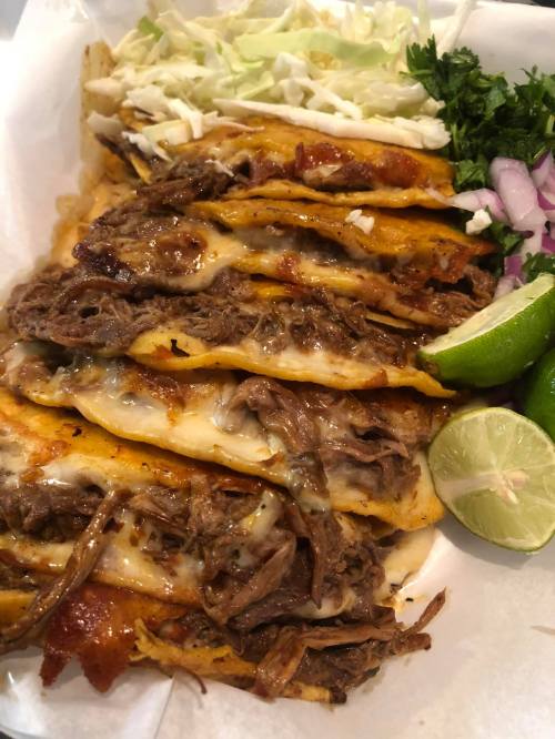 A plate of cheesy beef tacos topped with lettuce, onions, cilantro, and lime wedges.