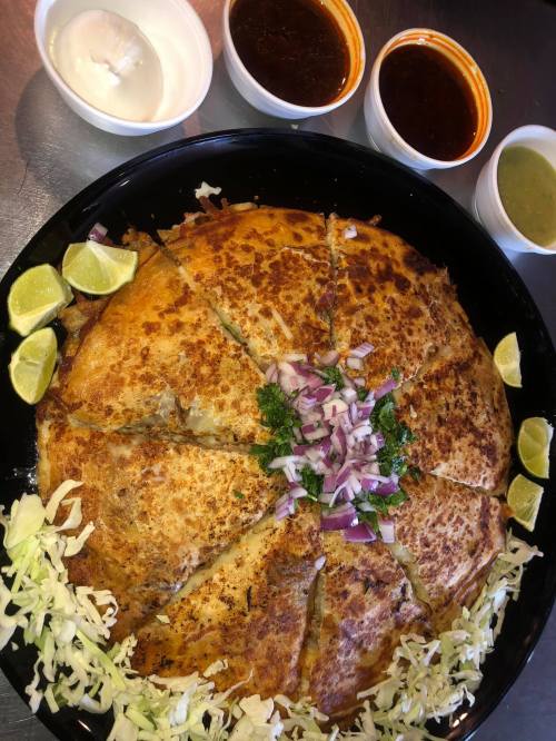 A large, golden-brown dish cut into wedges, garnished with onions and cilantro, served with four small bowls of sauces.