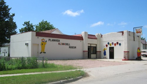 Exterior of the Plainview Klown Doll Museum, featuring colorful clown murals and a sign, set against a blue sky.