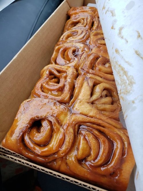 A box of freshly baked cinnamon rolls, glistening with a rich caramel glaze.