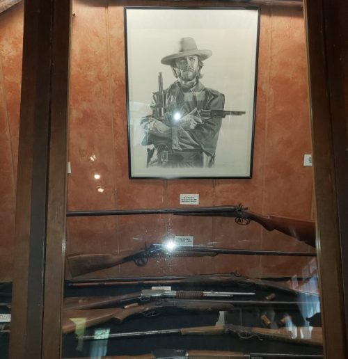 A display case featuring various rifles and a framed portrait of a cowboy holding a gun.