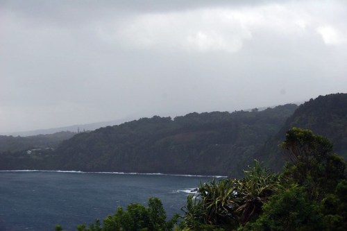 A misty coastal landscape with dark clouds, lush green hills, and waves crashing against the shore.