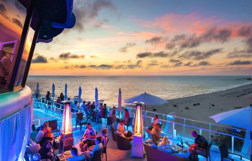 A vibrant beachside restaurant at sunset, with patrons enjoying the view and colorful lighting.