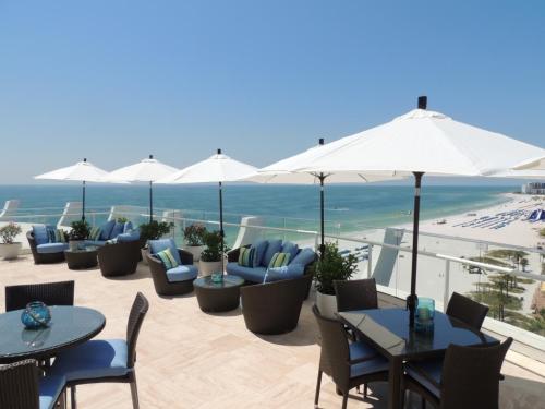 Rooftop lounge with blue seating, white umbrellas, and ocean view, overlooking a sandy beach and clear sky.