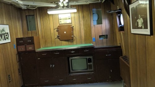 Interior of a wooden-paneled room featuring a green countertop, cabinets, a vintage TV, and framed photos on the walls.