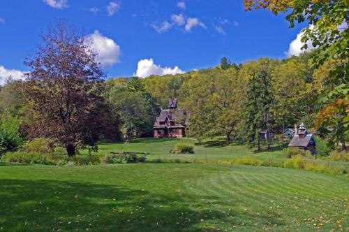 A scenic view of a green lawn with a rustic house and trees under a blue sky with fluffy clouds.