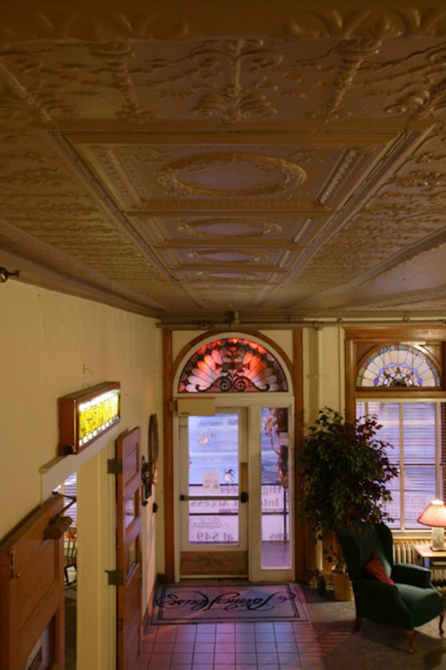 Interior view of a vintage hallway with ornate ceiling, decorative windows, and a cozy seating area.