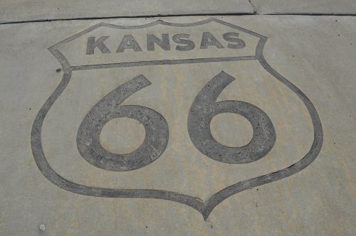 A concrete surface featuring a shield-shaped sign with "Kansas" and "66" inscribed on it.