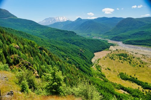 A lush green valley surrounded by mountains under a clear blue sky, with a river winding through the landscape.