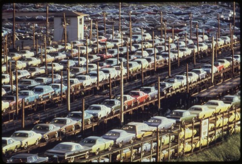 Aerial view of a large parking lot filled with rows of parked cars, showcasing various colors and models.