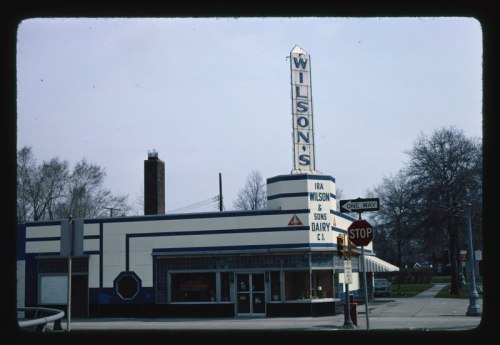 Historic Wilson's Dairy building with a tall sign, featuring a one-way street and stop sign in the foreground.