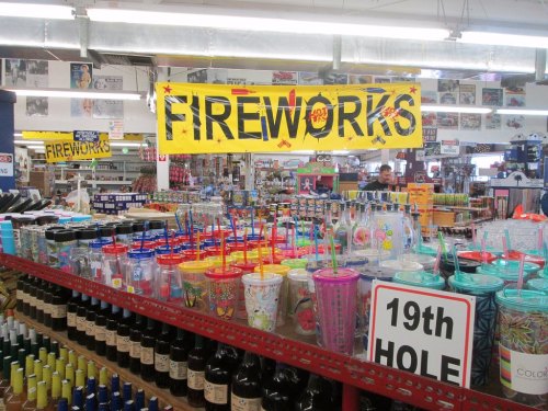 A colorful display of cups and fireworks signage in a store, with various products and customers in the background.