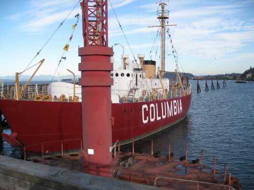 A red lighthouse ship named "Columbia" docked at a pier, with a clear blue sky and water in the background.