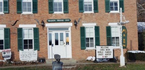 Historic brick building with green shutters, featuring signs for Mason House Inn and a ghost hunter event.