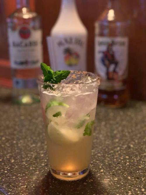 A refreshing cocktail with mint and lime, served in a glass, with bottles of liquor blurred in the background.