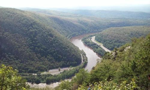 A scenic view of a winding river surrounded by lush green mountains under a clear sky.