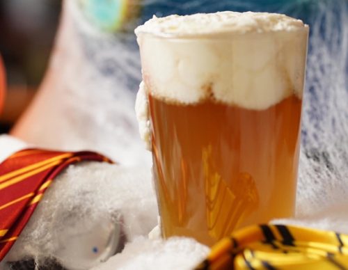 A frothy beer in a glass, surrounded by festive decorations and a colorful background.