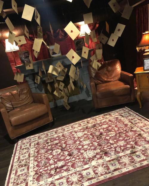 Cozy room with two leather chairs, a patterned rug, and letters hanging from the ceiling against a dark backdrop.