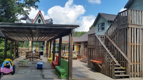 Playground area with colorful seating, a wooden structure, and a staircase leading to a building under a blue sky.