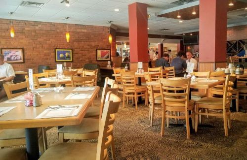 A spacious restaurant interior with wooden tables and chairs, featuring a few diners and warm lighting.