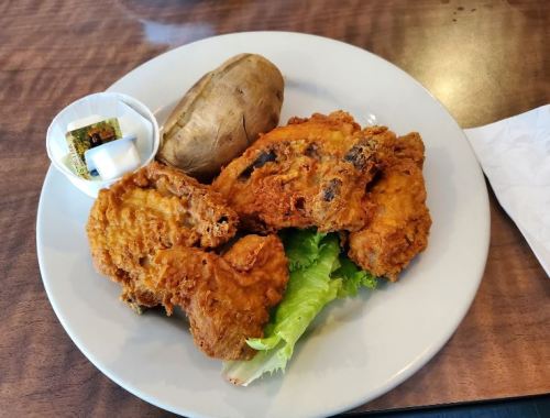 A plate with fried chicken, a baked potato, and a small cup of butter on a bed of lettuce.
