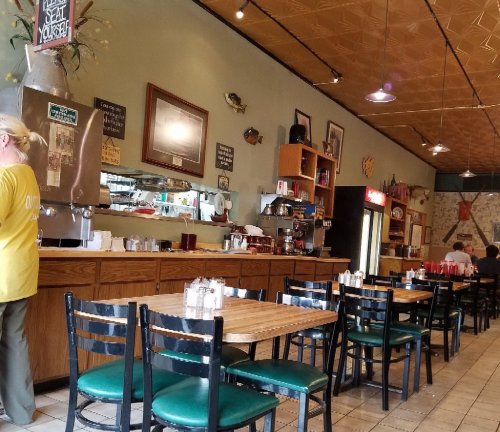 A cozy diner interior with wooden tables, green chairs, and a counter with drinks and condiments.