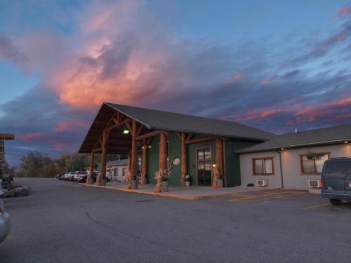 A rustic lodge with a wooden entrance under a colorful sunset sky, surrounded by parked cars.