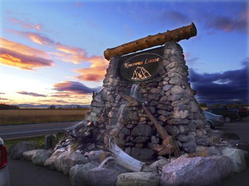A stone sign for "Ninety-Nine Lodge" with a waterfall feature, set against a colorful sunset sky.