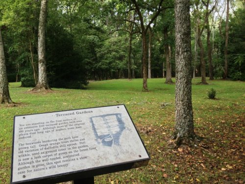 A sign in a wooded area describes the terraced gardens, surrounded by trees and lush greenery.