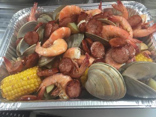 A tray filled with shrimp, clams, sausage, corn, and vegetables, all seasoned and cooked together.