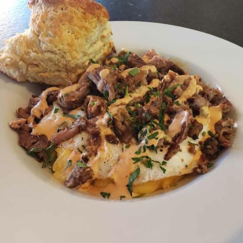 A plate of hearty breakfast featuring scrambled eggs, seasoned beef, drizzled sauce, and a biscuit on the side.