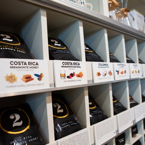 Coffee bags displayed on shelves, labeled with origins and tasting notes, including Costa Rica and Colombia varieties.