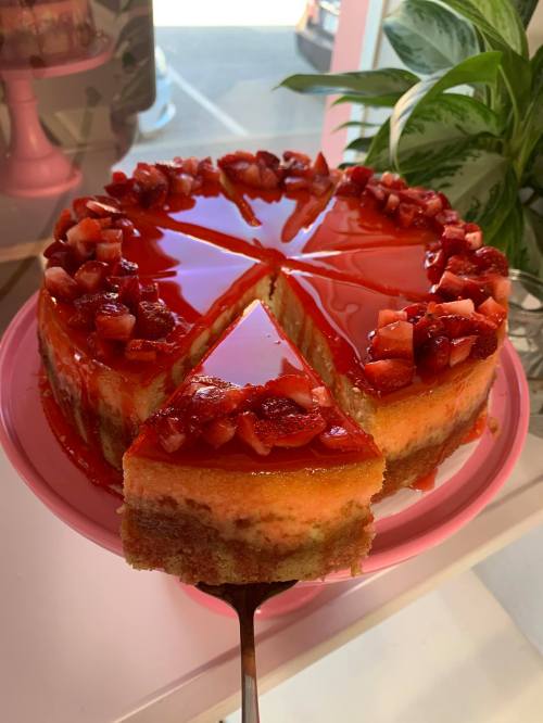 A slice of strawberry cheesecake on a pink plate, topped with fresh strawberries and a glossy red glaze.