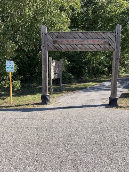 Wooden entrance sign for Pathfinder Park, with a path leading into a wooded area and a signpost nearby.