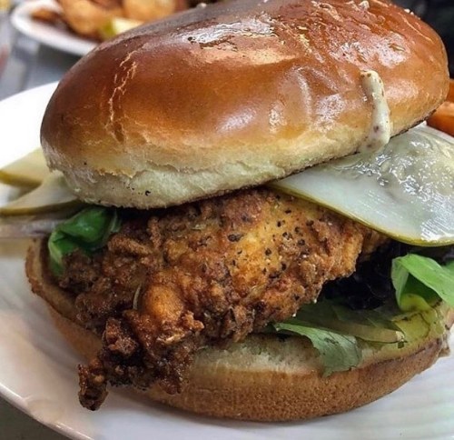 A crispy fried chicken sandwich with pickles and lettuce on a toasted bun, served on a white plate.