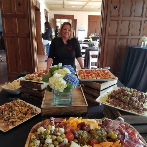 A chef stands behind a beautifully arranged buffet table with various dishes and floral centerpieces.