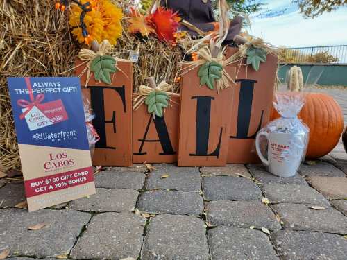 Decorative fall display with wooden letters spelling "FALL," a pumpkin, and a promotional sign for Los Cabos gift cards.