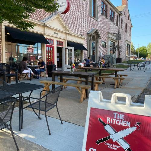 Outdoor seating area of Cherry Street Kitchen, featuring tables, chairs, and a sign in front of a brick building.