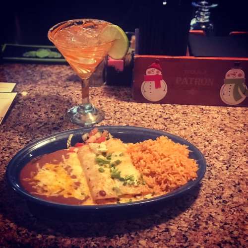 A plate of enchiladas with rice and salad, accompanied by a colorful cocktail with a lime wedge.