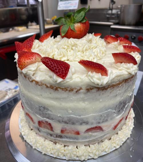 A layered cake topped with whipped cream and fresh strawberries, featuring a decorative border of cream.