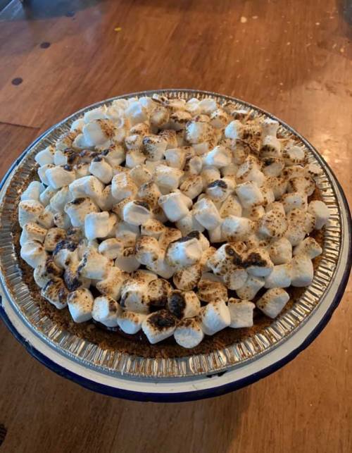 A pie topped with toasted mini marshmallows, sitting on a wooden table.