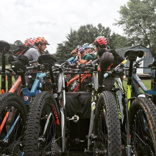 A group of mountain bikes lined up on a truck, with riders preparing for a biking adventure in a green outdoor setting.