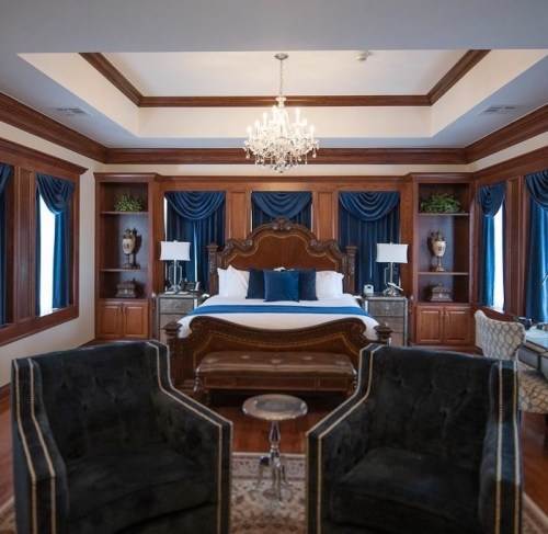 Elegant bedroom with a wooden bed, blue accents, a chandelier, and two plush black chairs.