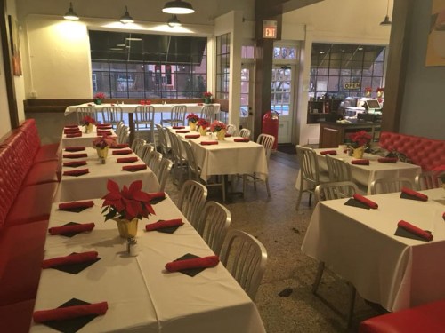 A cozy restaurant interior with red booths, white tables set with black napkins, and festive decorations.