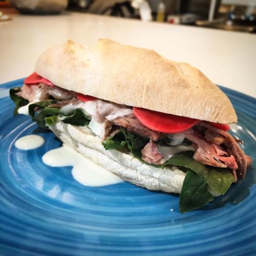 A delicious sandwich on a blue plate, filled with roast beef, lettuce, tomatoes, and a creamy sauce.