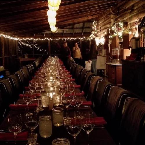 A long dining table set with glasses and candles, surrounded by warm lighting in a rustic, cozy space.