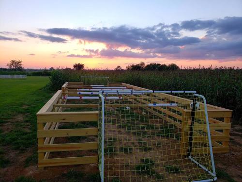 A wooden foosball table set outdoors, with goals, surrounded by tall grass and a colorful sunset in the background.
