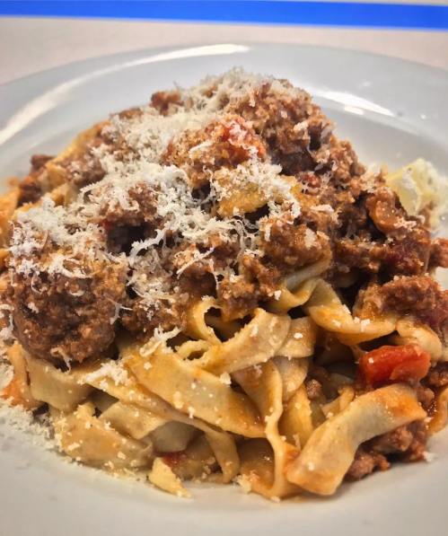 A plate of fettuccine pasta topped with a rich meat sauce and grated cheese.