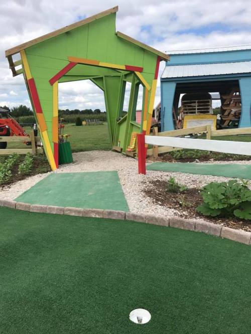 Colorful miniature golf entrance with a green and yellow structure, surrounded by grass and gravel pathways.