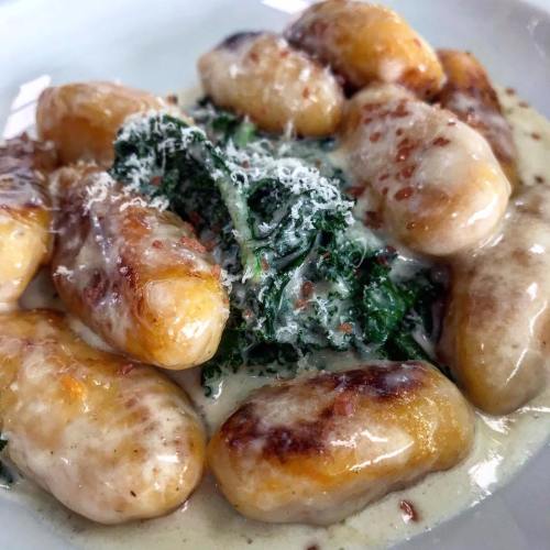 Plate of golden gnocchi topped with creamy sauce and fresh greens, sprinkled with grated cheese.